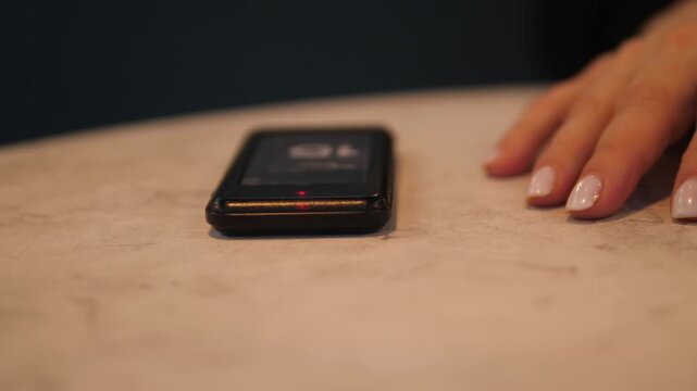 Electronic Queue System: A pager for notifying the customer when their order is ready. Side view of a guest pager and a visitor's hand resting on a table.