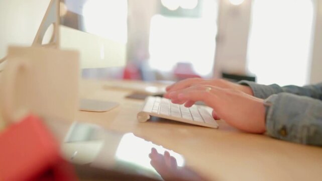 Creative freelancer working remotely on a desktop computer and digital tablet at a sunlit wooden desk.
