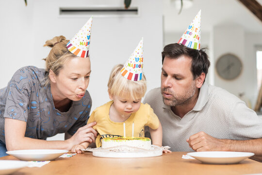 Joyful family birthday party with cake. Happy family celebrating their toddler's birthday at home with a cake and party hats.