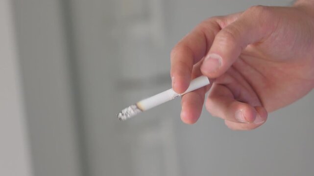 Detailed close-up of a person holding a lit cigarette with visible smoke, representing smoking addiction, tobacco use, nicotine dependence, unhealthy lifestyle, and lung disease risks.