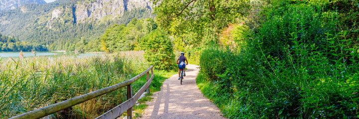 Obraz premium Biker rides along path by lake surrounded by trees and hills on sunny day