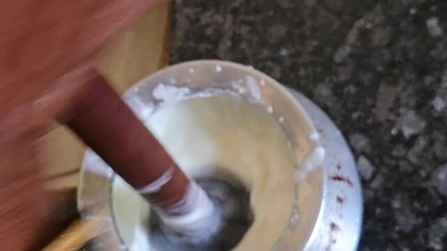 The traditional Bilona method: a wooden Madhani whisking curd in a metal pot. This rhythmic process creates frothy lassi or churns fresh butter, preserving authentic Indian heritage and local flavor.