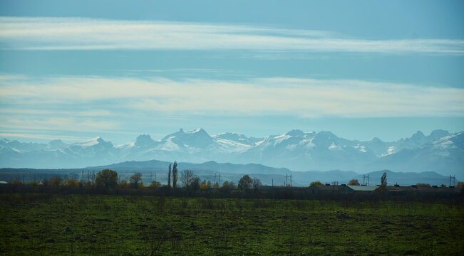 Early morning in autumn. In the distance, a settlement and the high mountains of the Caucasus