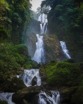 View of Curug Sewu Waterfall cascading through lush tropical forest and mossy rocks Kecamatan Patean, East Java, Indonesia.