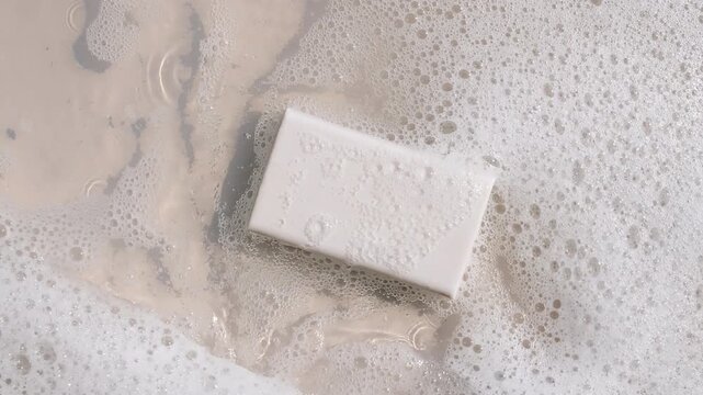 A bar of soap on a water surface with bubbles of white soapy foam. Concept of bath products, skin care products advertisement spa cosmetics. Body care and relaxation. High quality 4k footage