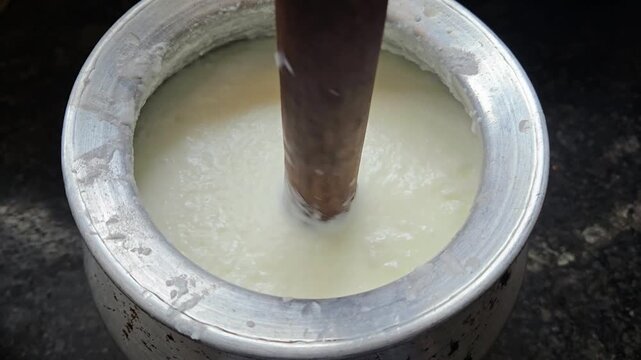 Traditional Bilona method: A wooden Madhani churner is hand-rotated in a metal pot to blend curd into frothy lassi or separate fresh butter, preserving authentic taste and nutrition in rural India.