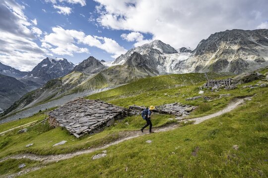Mountaineers on a hiking trail, Alpine huts covered with slate slabs, mountain landscape near Arolla, behind mountain peak Mont Collon and glacier Glacier de Tsijore Nouve, Valais, Western Alps Switzerland