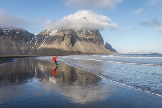 Man runs in a good mood on a black sandy beach, mountains Klifatindur, Eystrahorn and Kambhorn, headland Stokksnes, mountain range Klifatindur, Austurland, East Iceland, Iceland