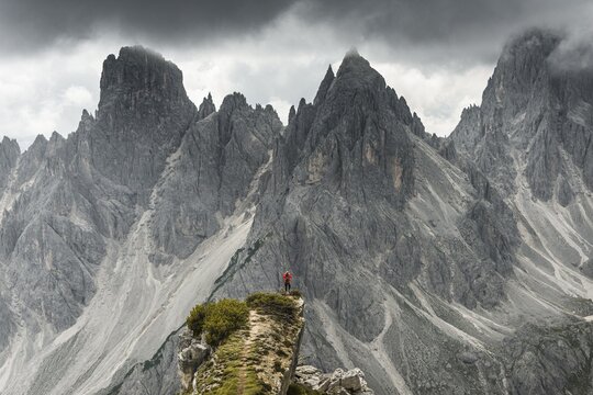 Man with red jacket standing on one degree, behind him mountain peaks and pointed rocks, dramatic clouds, Cimon the Croda Liscia and Cadini group, Auronzo di Cadore, Belluno, Italy