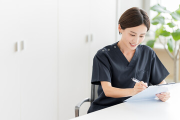 Naklejka premium 診察室でカウンセリングをしながらカルテを記入する日本人女性医師