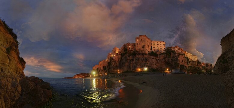 Panorama on the beach Lido Le Roccette Club Tropea with the old town of Tropea perched on sandstone cliffs and the sky lit up with clouds at sunset, Tropea, Vibo Valentia, Calabria, Southern Italy, Italy