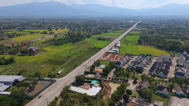 Robotic tracking shot moving backward over a growing town Features a primary road corridor residential developments and green farming zones toward misty hills in a wide eastern territory