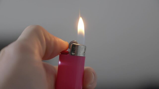 Lighting up a flint-wheel lighter with his thumb while holding it in his hand, closeup