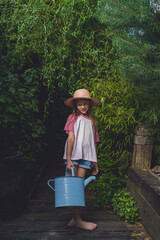 Fototapeta premium Little girl holding watering can in lush garden pathway.