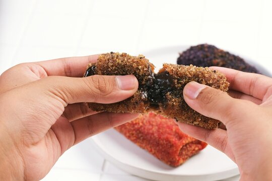 Close up of hands breaking crispy chocolate risoles showing soft filling inside. Popular Indonesian street food snack with crunchy texture and savory taste.