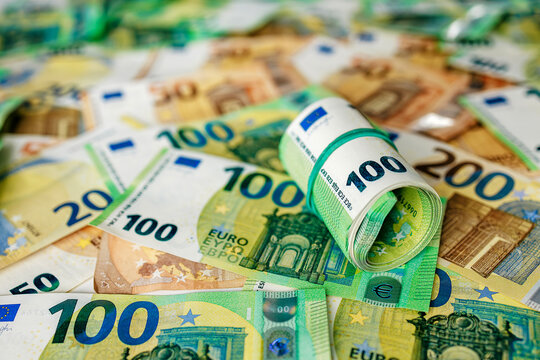Detailed view of rolled 100 euro banknotes held together with a rubber band placed on mixed euro currency background. Concept banking, money management and economy.
