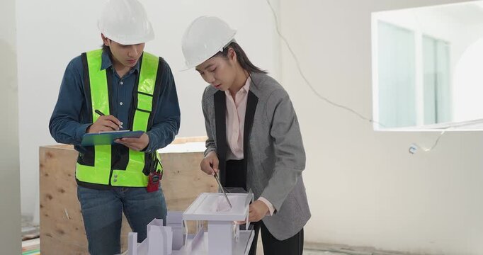 Male engineer and female architect review a building model, blueprints and a digital device at a residential construction site, planning design coordination and project development.
