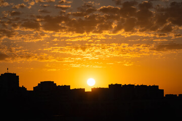 Naklejka premium Stunning golden sunset over Oismae residential district in Tallinn Estonia with dramatic sun disk above city building silhouettes and beautiful altocumulus clouds.