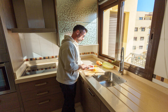 Man cooking healthy meal in bright kitchen, chopping fresh produce on cutting board with natural light