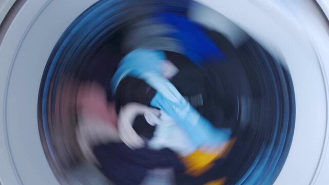 Overhead view of colorful clothes spinning inside a top-loading washing machine drum, speed ramping from slow to fast motion.