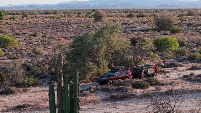 An SUV towing a teardrop camper trailer is parked at a dispersed camping site in Baja California Mexico by the ocean.