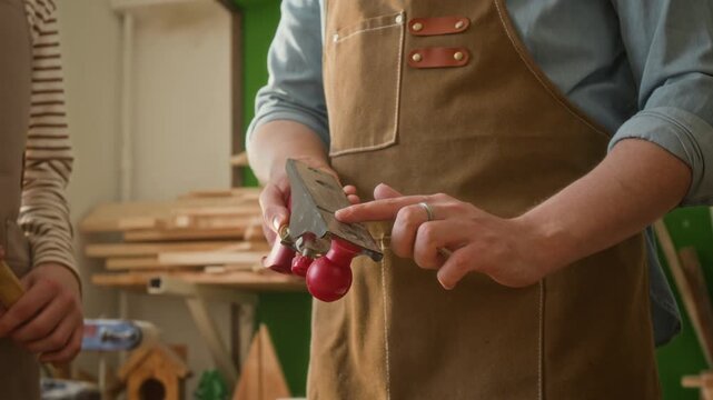 Midsection shot of unrecognisable craftsman wearing apron explaining how to work with hand plane to anonymous teenager holding hammer