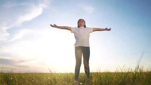 The free child's arms are looking to the sky. Religion freedom unity with nature concept. Girl in nature and religion with the sun. Girl child praying hands lifestyle to sides looking up in nature.