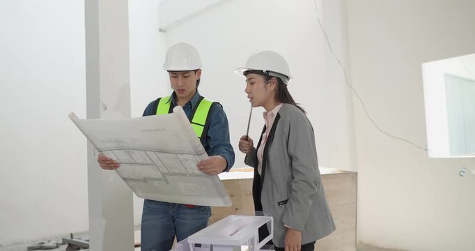 Male engineer and female architect review a building model, blueprints and a digital device at a residential construction site, planning design coordination and project development.
