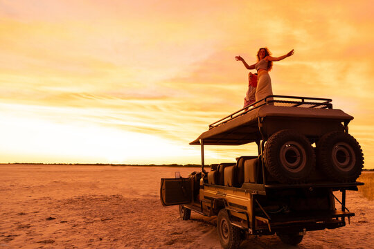 teen girl dancing atop safari vehicle at dusk, Makgadikgadi Park, Botswana, Africa