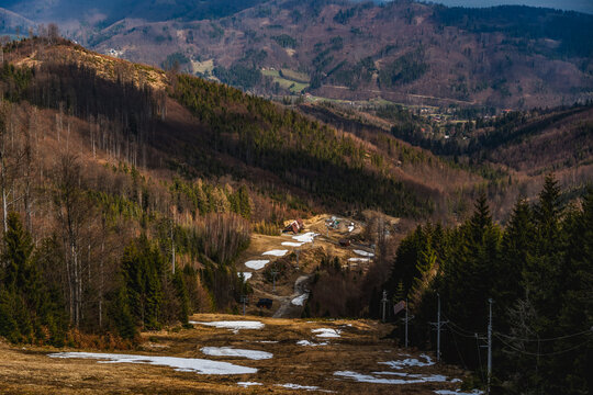 Spring mountain landscape with remaining snow patches on a ski slope surrounded by forested hills in the Beskid Mountains.