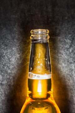 Closeup of clear glass beer bottle with cold beer against a black leather background