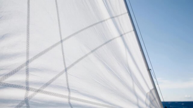 Close up of white sail on a sailboat against clear blue sky over calm ocean water