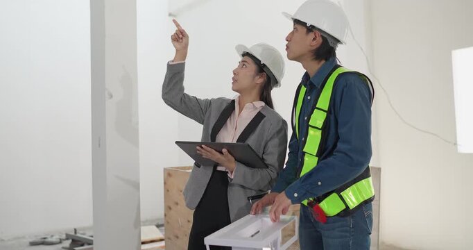 Male engineer and female architect review a building model, blueprints and a digital device at a residential construction site, planning design coordination and project development.
