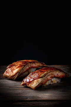 shot of a glazed Anago sea eel sushi at a 45 degree angle on a dark wooden surface. Muted natural color tones and hand-sliced uneven edges. Handcrafted rice with visible grains and handcrafted 