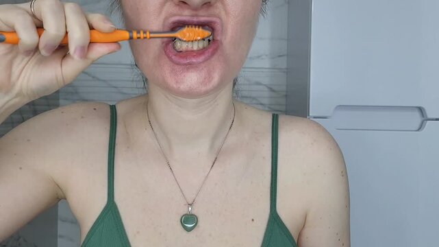 Side view of a woman brushing teeth in the bathroom, oral care habit and morning hygiene ritual
