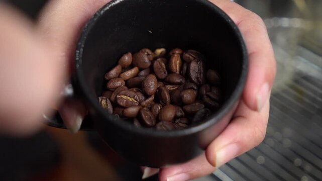 Closeup shot of a barista using a spray bottle to apply water to roasted coffee beans before grinding. This technique reduces static electricity for a professional workflow
