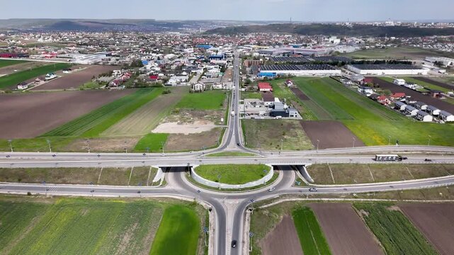 Aerial drone view of large roundabout and overpass at Suceava city entrance with traffic and surrounding farmland in Romania
