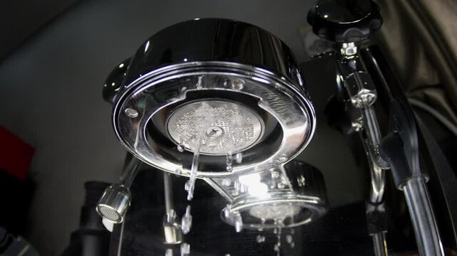 Close-up from below shows hot water dripping and flushing from a professional coffee machine group head. Ideal for content regarding equipment maintenance or cafe operations