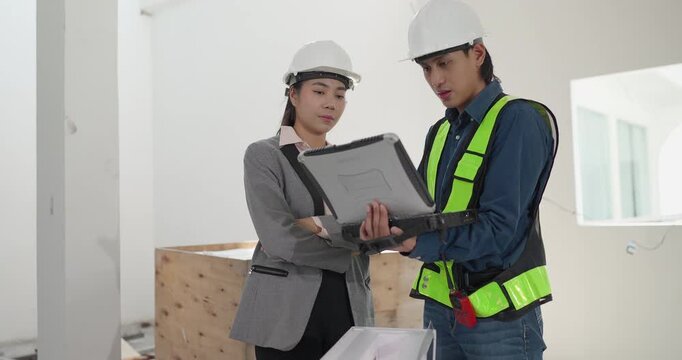 Male engineer and female architect review a building model, blueprints and a digital device at a residential construction site, planning design coordination and project development.
