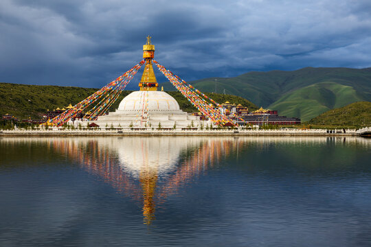 Stupa at the Zhuqing Wujian Zen Forest Monastery, decorated with prayer flags, reflections in the calm lake water.