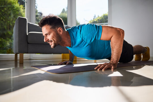 Man doing pushups on mat in sunny living room at home