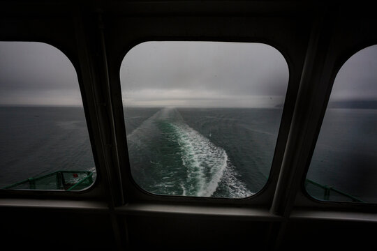 View through a ferry porthole window of the grey stormy weather in the San Juan Islands and the boat wake.