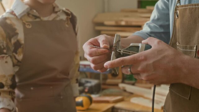 Midsection view of unknown craftsman inserting jigsaw blade before anonymous teenage girl checking its sharpness