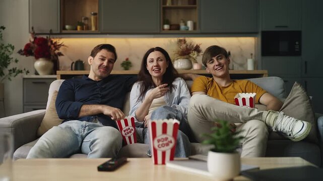 Teenage boy and his parents watching a movie and eating popcorn, family pastime