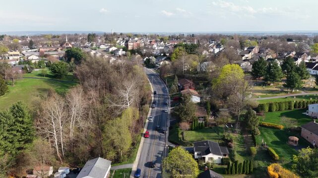 Aerial establishing shot of well kept suburb neighborhood during sunset time in America. Blooming trees in spring. Rising shot. Cars on Main Street. Wide shot. Pennsylvania, USA.