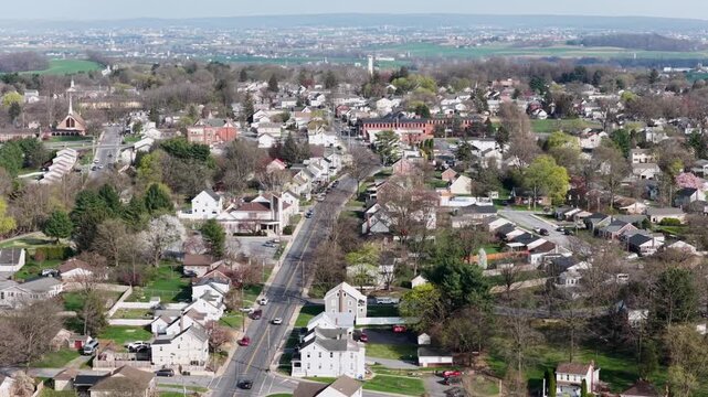 Aerial drone view of Akron Pennsylvania on sunny spring day with residential neighborhoods, main road traffic, trees and suburban homes in peaceful small town USA landscape. Wide shot.