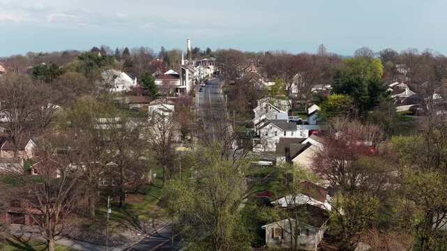 Aerial drone view of residential street in Akron, Pennsylvania, United States, with suburban homes, light traffic and early spring foliage in quiet small-town American setting.