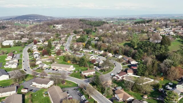 Quiet suburban neighborhood in Akron, Pennsylvania with curving streets, detached homes and early spring trees, light traffic and open green spaces under soft daylight. Aerial wide view.