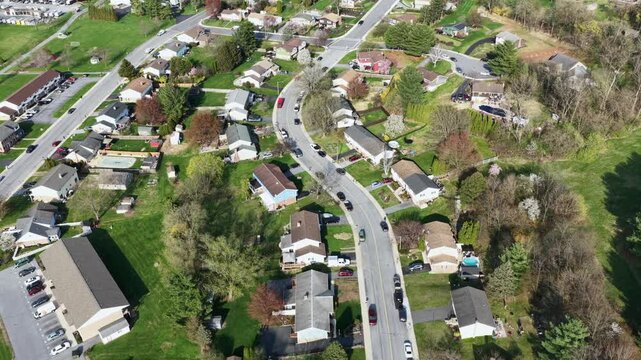 Aerial flyover of quiet suburban neighborhood in Akron,Pennsylvania, with curved residential streets, traditional homes, green spring lawns, trees and peaceful small town community on sunny day.