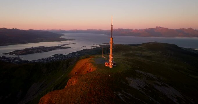 Orbiting aerial at golden hour around Stokmarknes TV and radio tower on Storheia
